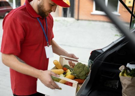 mężczyzna wkładająca skrzynkę z warzywami do bagażnika samochodowego