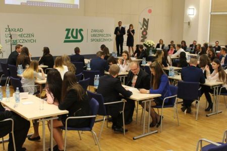 Uczniowie siedzący w ławkach i słuchający prowadzącego pracownika ZUS