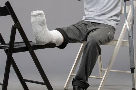 Osoba pisząca na krześle ze stopą w gipsie