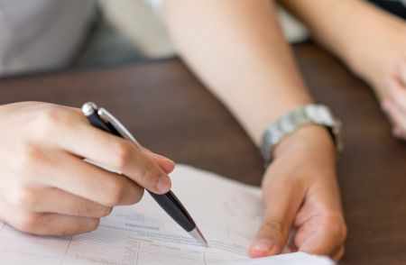 Osoba wypełniająca coś w wersji papierowej długopisem